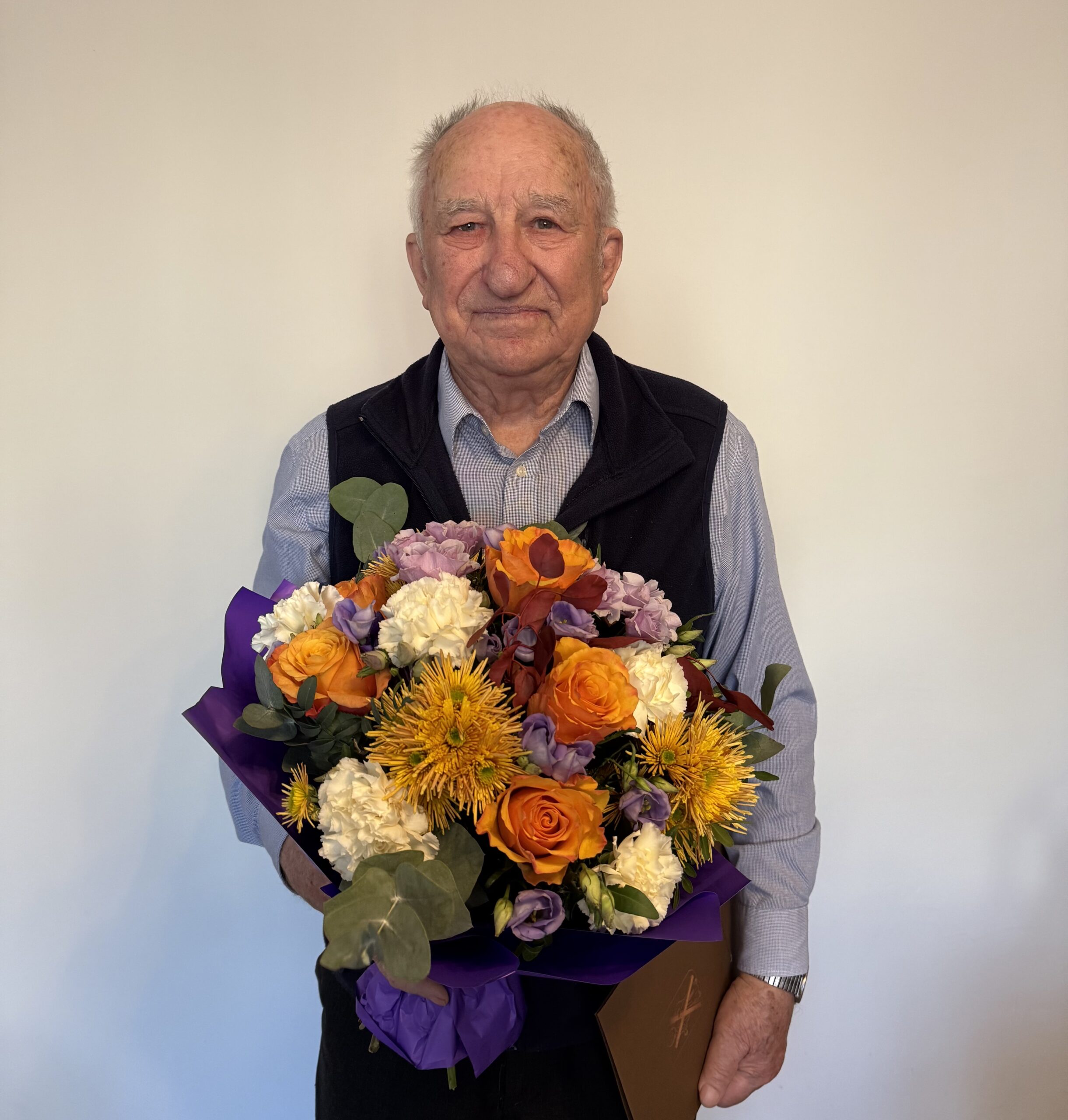 Na fotografii jubilat, który pozuje z bukietem kwiatów i listem gratulacyjnym.