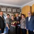 Grupowe zdjęcie, na którym jest wójt, kierownik USC oraz jubilaci wraz ze swoimi dwiema córkami. Jubilatka pozuje z bukietem kwiatów, a jubilat z upominkiem - książką o gminie.