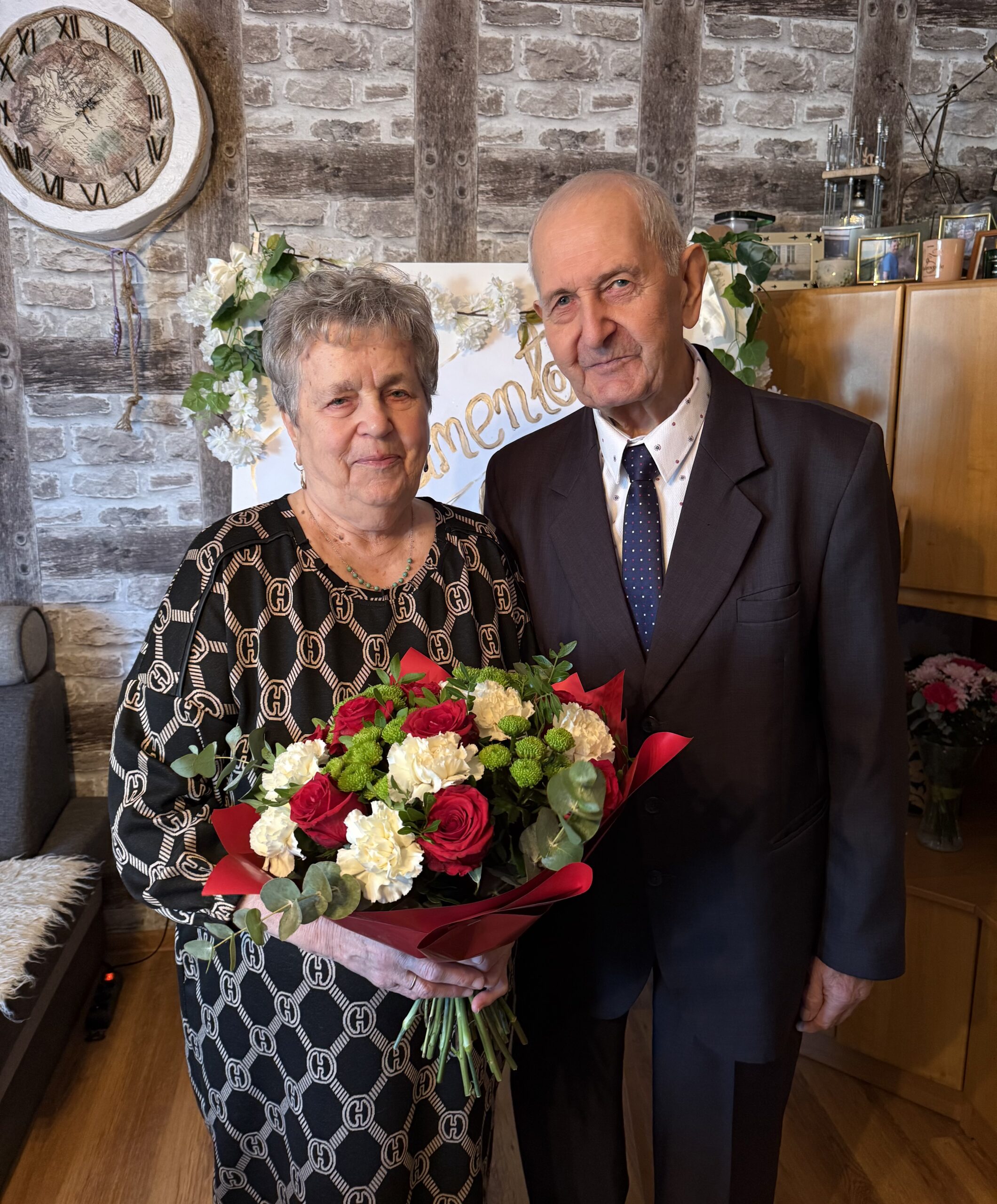 Wspólne zdjęcie jubilatów. Kobieta pozuje z bukietem kwiatów.