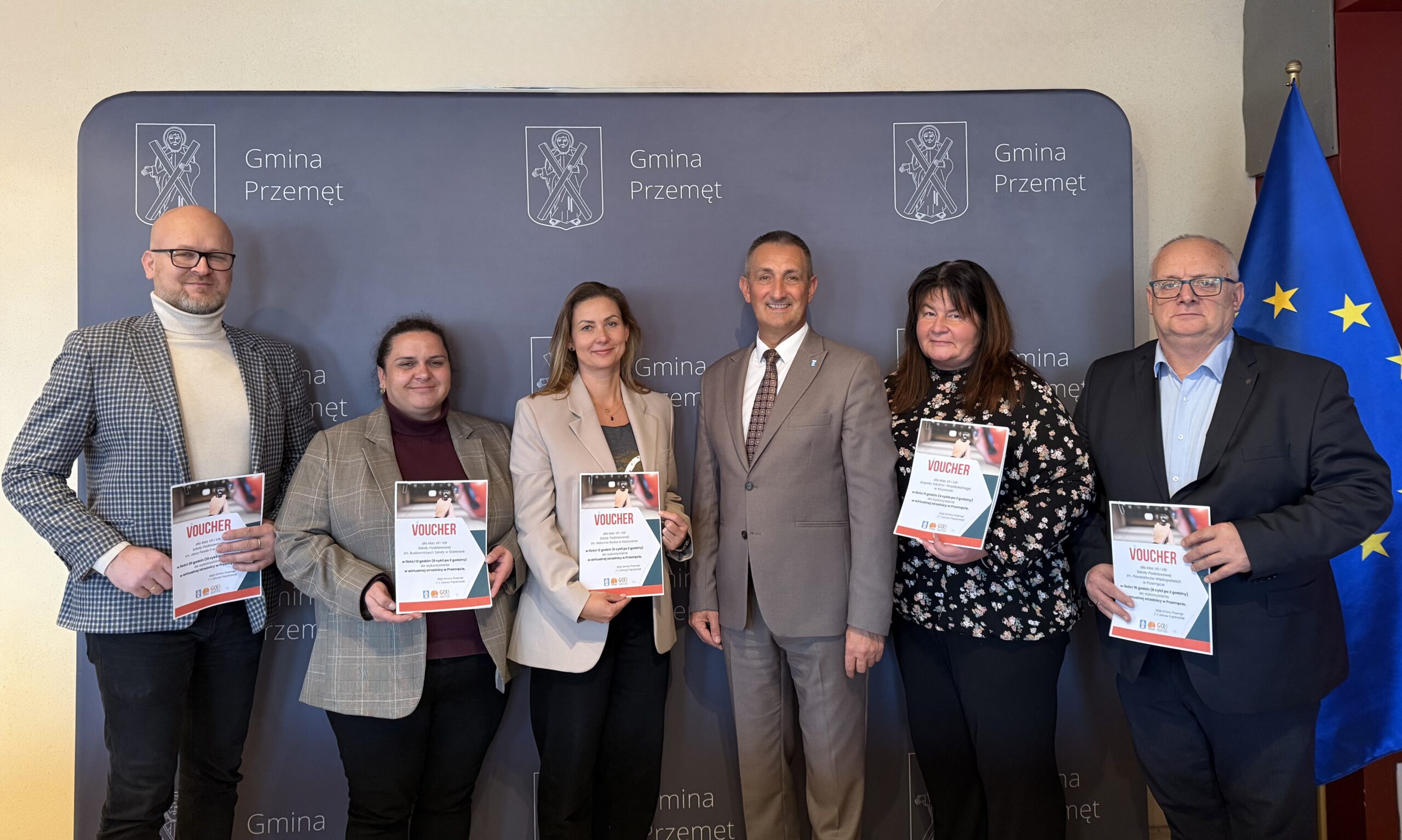 Na zdjęciu wójt wraz z dyrektorami szkół. Dyrektorzy pozują z voucherami. W tle ścianka gminy Przemęt.