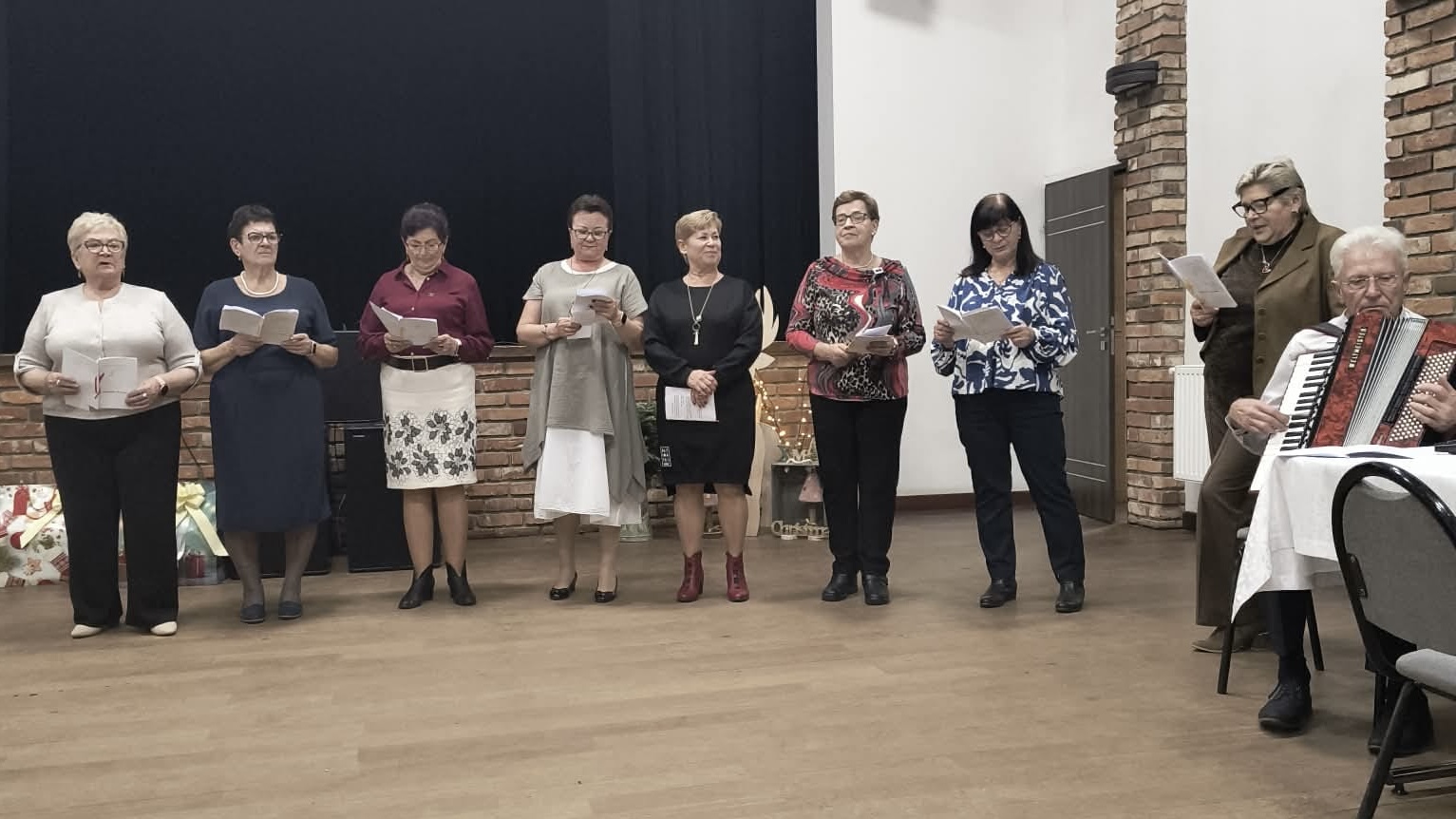 Na zdjęciu widoczne kobiety z UTW, które śpiewają oraz jeden mężczyzna, który przygrywa im na akordeonie.