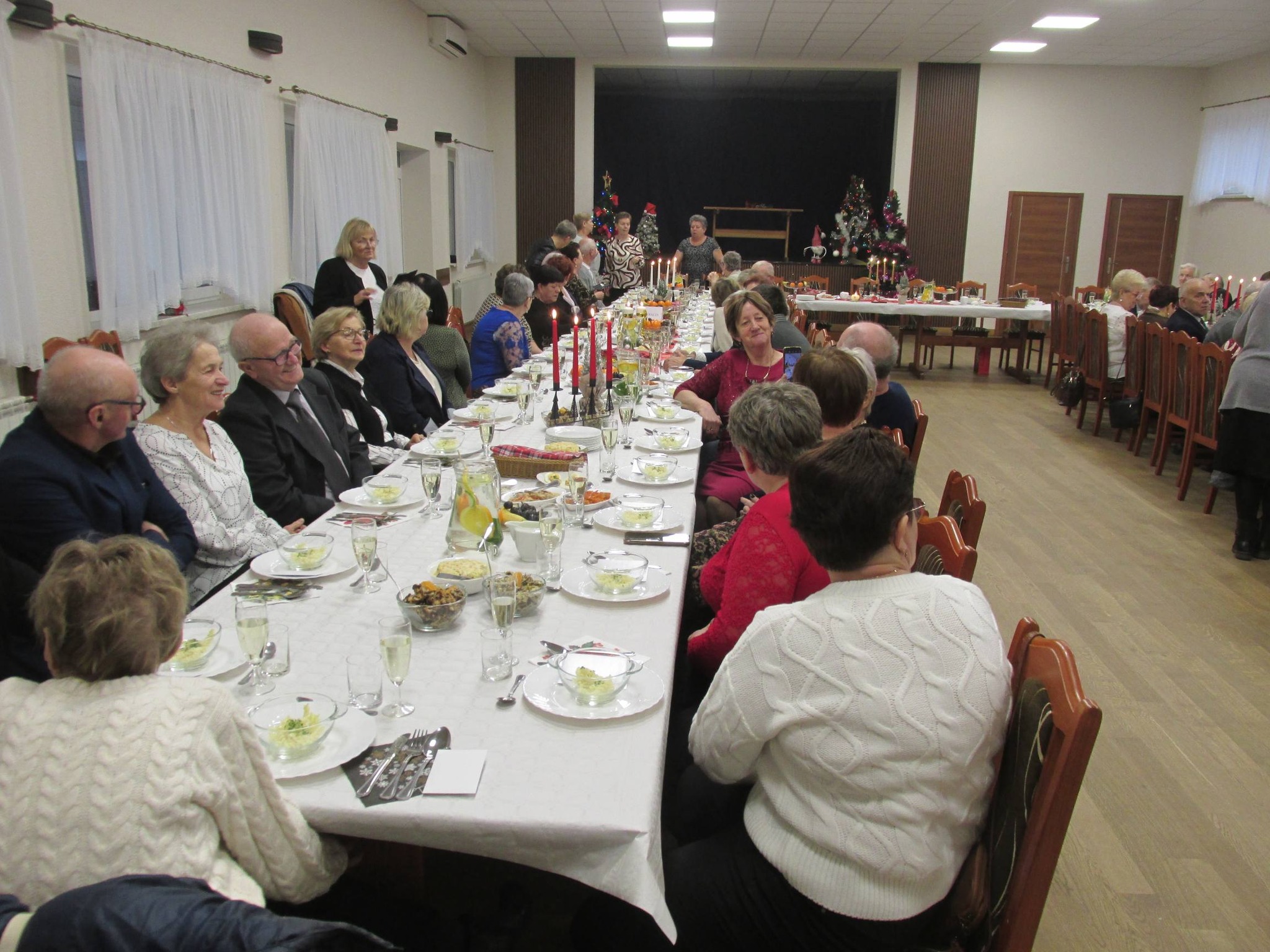 Na zdjęciu widoczni seniorzy, którzy siedzą przy stołach w trakcie spotkania wigilijnego.
