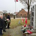 Na fotografii widoczna jest delegacja oddająca hołd powstańcom przy pomniku w Kaszczorze. Pan Robert trzyma wiązankę, wójt i pan Antoni stoją obok.