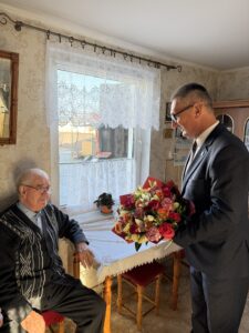 Na fotografii widoczny wójt, który wręcza jubilatowi bukiet kwiatów.