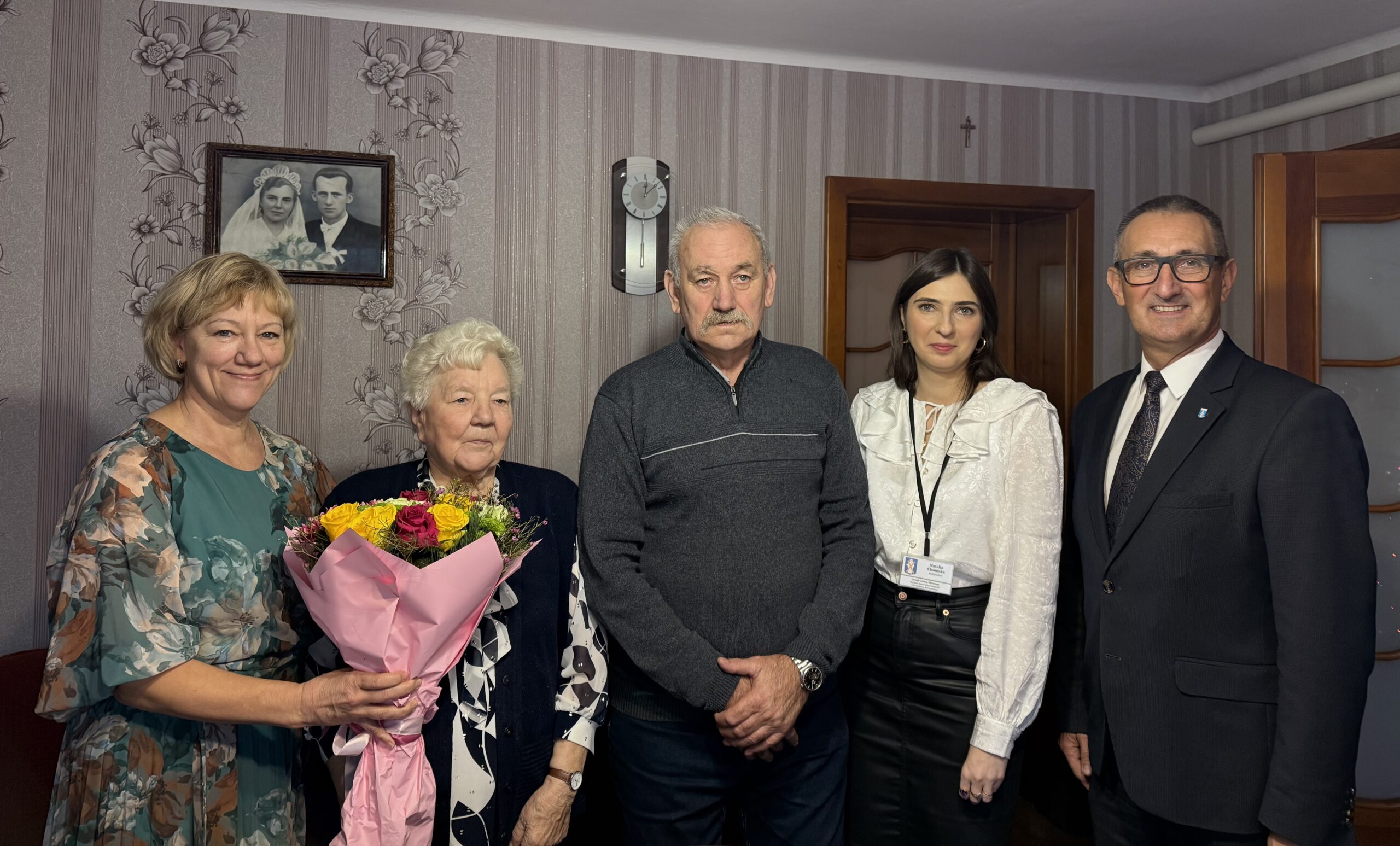 Na zdjęciu wójt Janusz Frąckowiak, pracownik USC Natalia Chomska oraz jubilatka wraz z bliskimi z rodziny. Jubilatka pozuje z bukietem kwiatów.