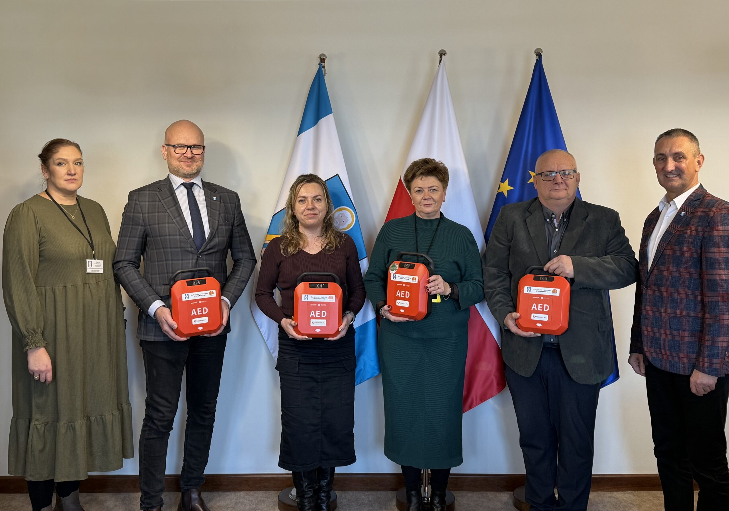 Na fotografii dyrektorzy szkół wraz z wójtem i kierownikiem oświaty i sportu. Dyrektorzy pozują z urządzeniami AED.